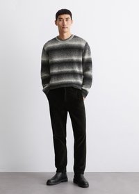 Grau- und schwarzgestreifter Pullover aus strukturiertem Strick, kombiniert mit schwarzer Cordhose und klobigen schwarzen Stiefeln. Schlichtes, modernes Design.