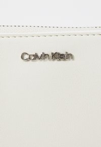 Portafoglio in pelle bianca testurizzata con il logo "Calvin Klein" in argento, con cuciture dettagliate lungo i bordi.