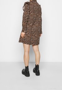 Leopardmönstrad klänning i brunt och svart med skräddarsydd passform, långa ärmar och hög krage; ihop med svarta ankelstövlar.