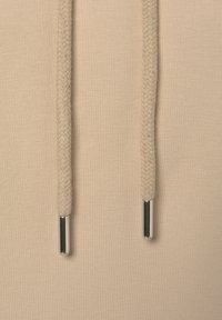 Felpa beige con cordini intrecciati, punte in metallo argentato e una texture di cotone liscia, che mette in mostra un design semplice e minimalista.