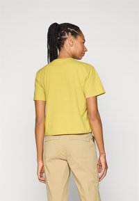 T-shirt gialla a maniche corte, realizzata in morbido cotone, presenta un collo rotondo e una vestibilità rilassata, abbinata a pantaloni cargo beige.