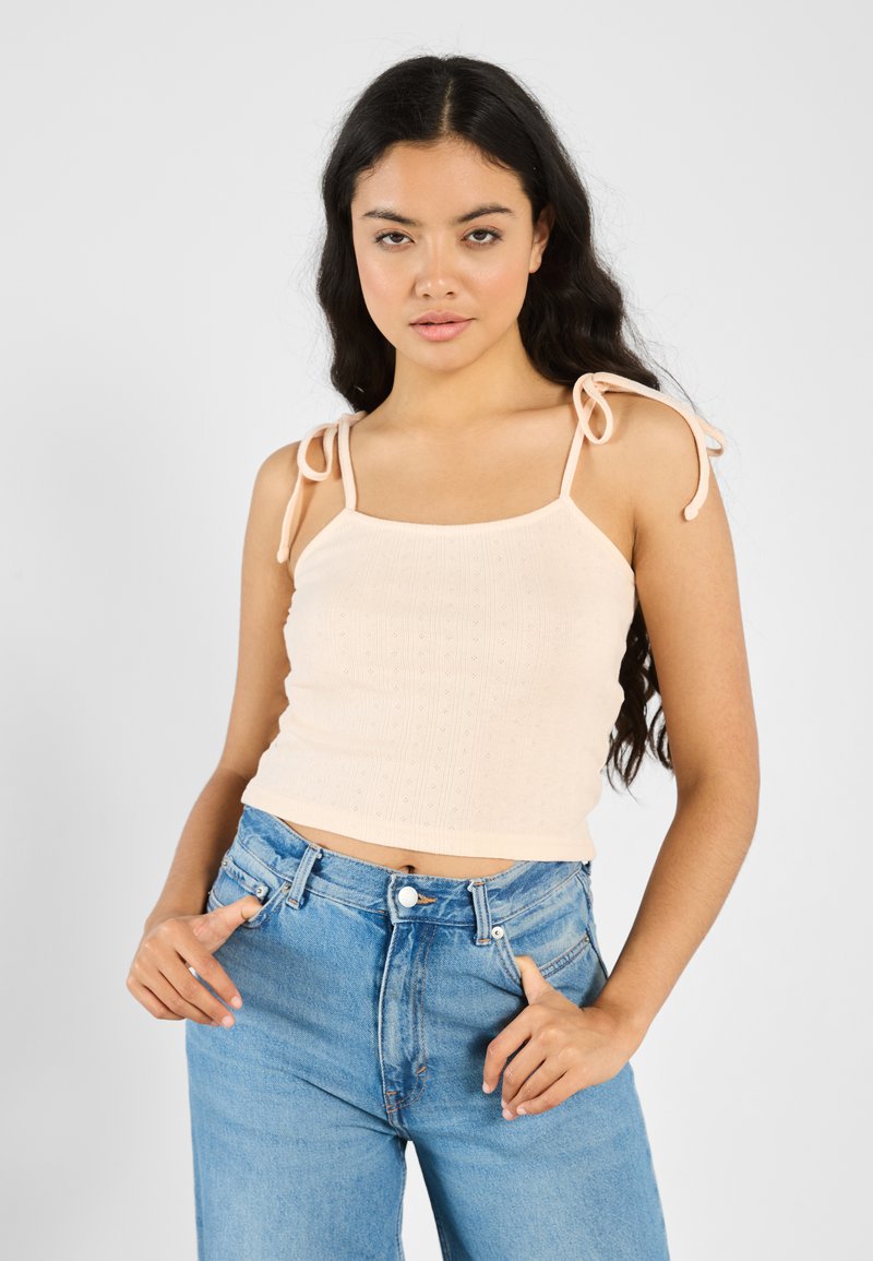 Lyserød ferskenfarvet, ribbet crop top med firkantet udskæring og bindebånd, parret med højtaljede lyseblå jeans. Casual tekstildesign.