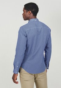 Blauw-witte gestreepte langemouwen shirt met een button-down kraag, gestructureerde stof en een gebogen zoom, gedragen met beige broeken.