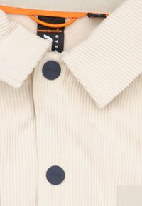 Beige corduroy overhemd met een knoopsluiting aan de voorkant, voorzien van marineblauwe knopen, een omgeslagen kraag en een oranje lusdetail bij de halsopening.