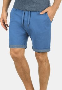 Shorts en coton bleu avec taille à cordon, ourlet retroussé et poches latérales. Tissu léger, texture lisse et design décontracté.