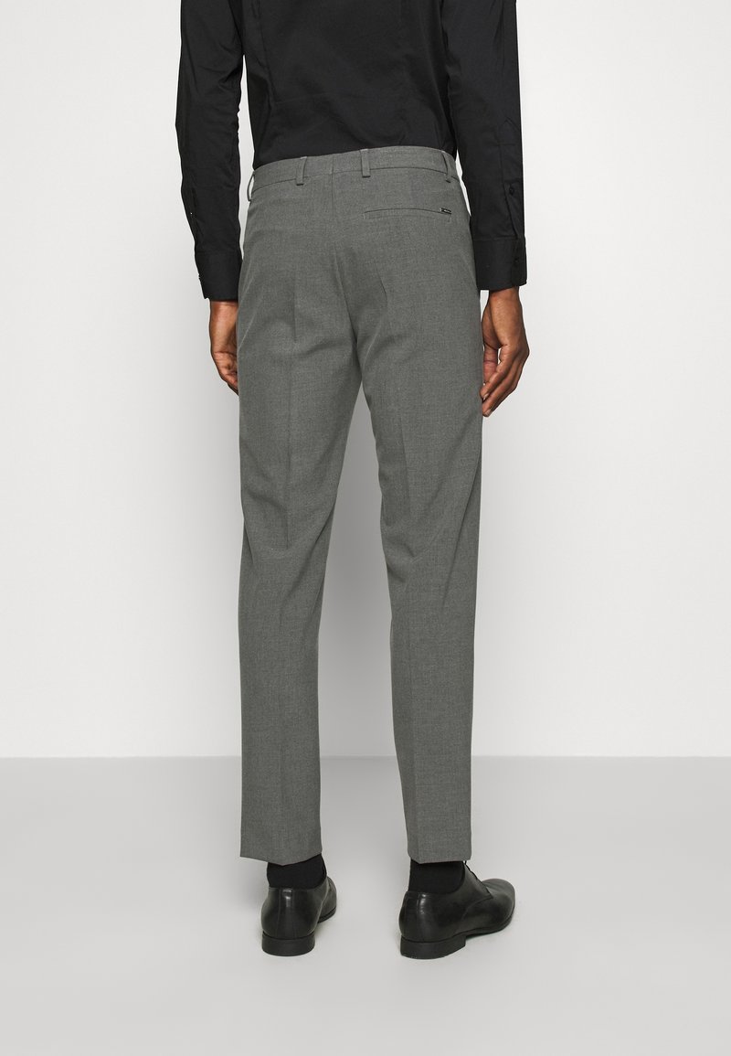 Pantaloni grigi su misura con una texture liscia, vestibilità slim e pieghe sottili. Indossati con scarpe nere e una camicia nera a maniche lunghe.