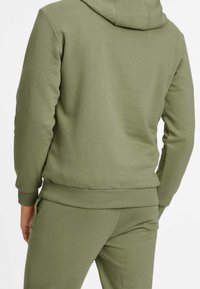 Sweat à capuche vert olive en tissu texturé, doté d'une capuche à cordon de serrage et de poignets côtelés. Design doux et décontracté, adapté à diverses occasions.