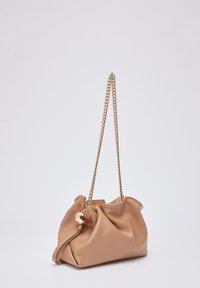 Sac à main en cuir fauve au design souple, avec une bandoulière chaîne dorée et un détail de fermoir hexagonal. Texture lisse et forme arrondie.