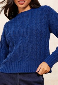 Pleteni moderni pulover v modri barvi z rečnimi detajli, rebrastimi manšeti in robom, mehko teksturo ter okroglim izrezom.