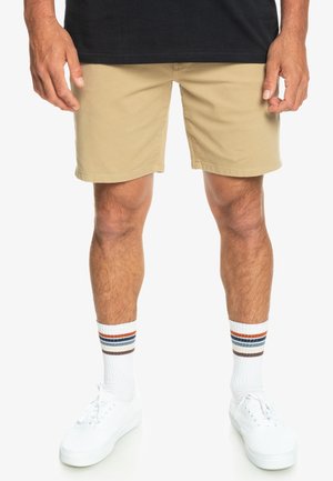 Beige cotton shorts with a straight cut, paired with white sneakers and striped white socks featuring red, blue, and gray accents.