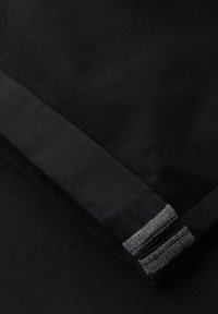 Primo piano di una manica in tessuto nero con risvolto piegato che presenta due toppe rettangolari grigie cucite.