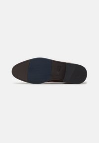 Suela de zapato marrón con una suela de goma que presenta un patrón texturizado en azul oscuro y un acento liso en goma negra. Branding sutil visible.
