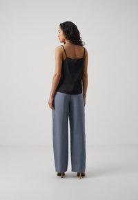Black satin camisole with thin straps, paired with loose, light blue wide-leg trousers. Yellow heels complete the look.