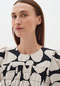 Topy s nariasenými rukávmi, krémová tkanina so čiernym abstraktným vzorom, zberné detaily na hrudníku, okrúhly výstrih, hladká textura.