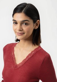 Rood geribbeld topje met een V-hals, gedetailleerde kantafwerking en lange mouwen. Gladde textuur en aansluitend ontwerp.