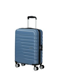 Valise rigide bleue avec des rainures horizontales, poignée télescopique, quatre roues pivotantes et serrure à combinaison. Texture lisse et design robuste.