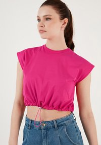 Fuchsia afskåret t-shirt med korte �ærmer, samlet talje og justerbar snoretræk. Sammen med højtaljede blå denim jeans.