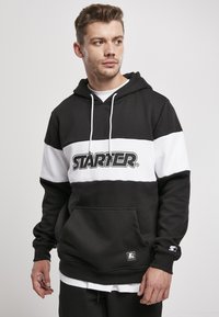 Černobílá mikina s kapucí, která má p�řední klokanní kapsu, pružné manžety a výrazné logo "STARTER" na hrudi.