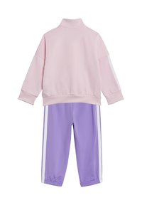 Ljusrosa zip-up-jacka med hög krage och vita ränder på ärmarna, i kombination med lila byxor med vita sidostripes. Mjuk tyg och avslappnad passform.