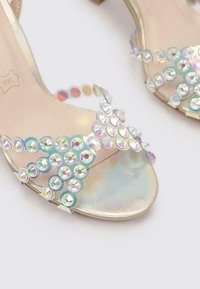 Zapatos de tacón abiertos con un acabado holográfico, presentando piedras brillantes transparentes dispuestas en un patrón ondulado a lo largo de las correas.