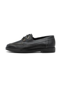 Scarpa da barca in pelle nera con punta rotonda, cuciture beige a contrasto e due occhietti dorati. Sole in gomma piatta per stabilità.
