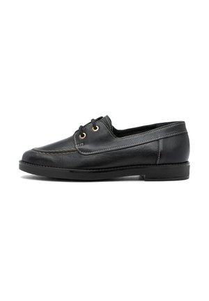 Scarpa da barca in pelle nera con punta rotonda, cuciture beige a contrasto e due occhietti dorati. Sole in gomma piatta per stabilità.
