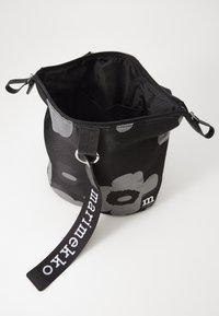 Black fabric bag with floral pattern in grey, featuring a top zipper, two handles, and a printed logo strap. Interior is plain black.
