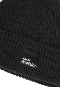 Berretto in maglia nera con texture a coste. Presenta un patch quadrato in tessuto con il logo "Jack Wolfskin" in bianco. Gli accenti conferiscono un aspetto aderente.