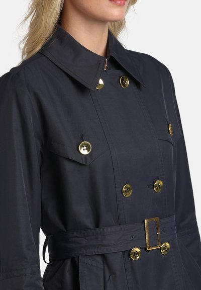 Trenci bleu marin cu guler, nasturi aurii, buzunare duble și talie cu curea. Confecționat dintr-un material neted, cu un design croitorit.