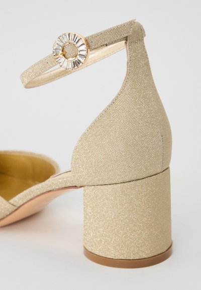 Goldglitzernde High-Heels mit rundem Zehenbereich, Knöchelriemen und dekorativer Strassschnalle. Verfügt über einen dicken, zylindrischen Absatz.