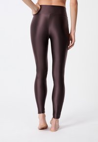 Leggings marrones de cintura alta hechos de un material brillante y elástico; diseño ajustado con una cinturilla sin costuras y corte hasta el tobillo.