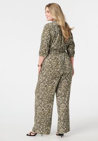Une combinaison à motifs verts et crème avec des manches courtes, une taille cintrée et des jambes larges. Le design présente des formes géométriques et une coupe décontractée.
