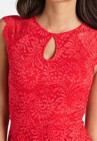 Röd spetklänning med korta ärmar och en nyckelhålsringning, med blommiga och bladmönster på tyget.