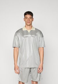 Grå trøye med en lysfarget krage, med et geometrisk mønster. "UMBRO F.C." trykt tydelig på forsiden. Sammen med matchende shorts.