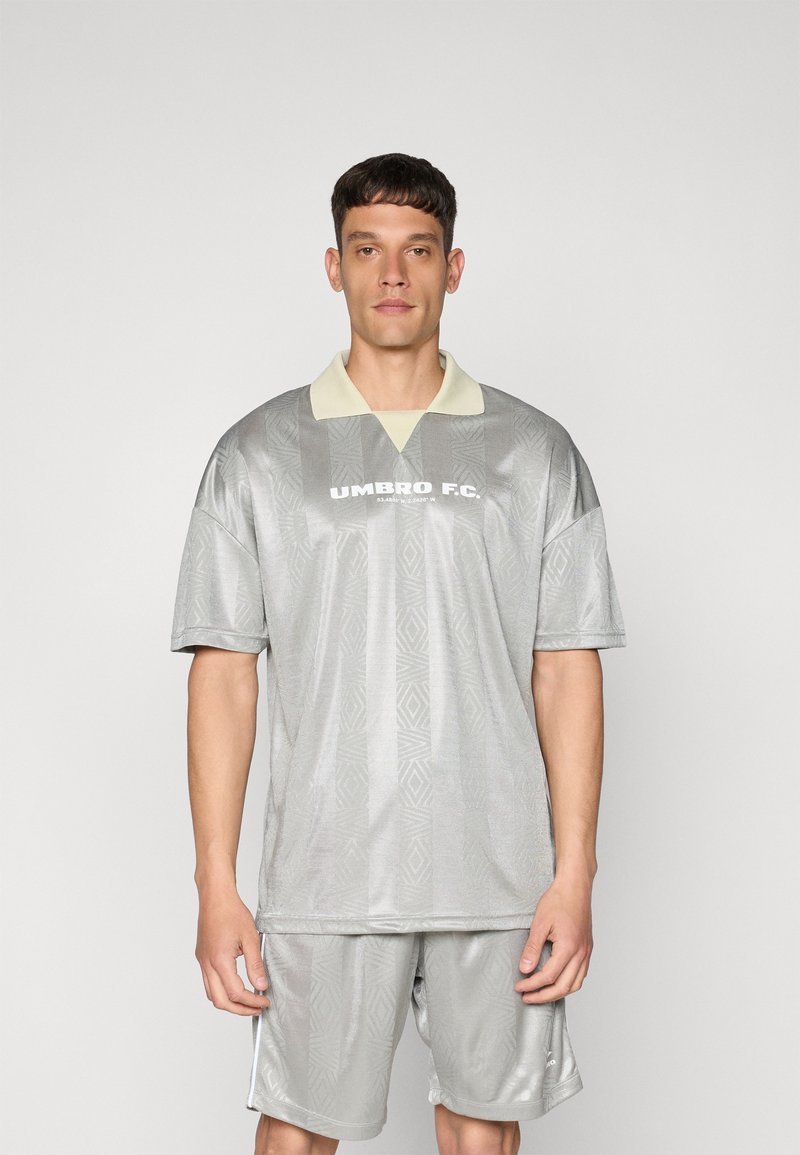 Grå trøye med en lysfarget krage, med et geometrisk mønster. "UMBRO F.C." trykt tydelig på forsiden. Sammen med matchende shorts.