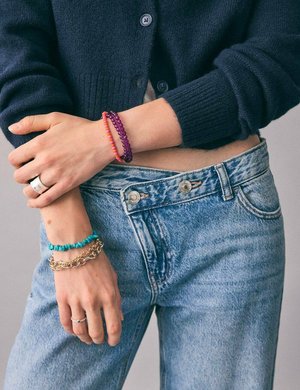 Jean en denim taille haute. Cardigan en tricot bleu, plusieurs bracelets en turquoise, or et violet. Les accessoires comprennent des perles et des chaînes.