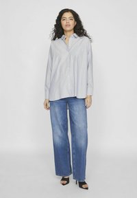 Camisa de botón a rayas azul claro con mangas largas y bolsillo en el pecho, combinada con jeans holgados azules y sandalias negras de tacón alto.
