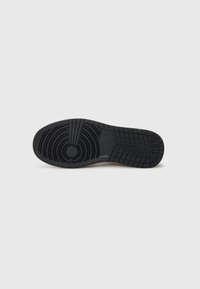 Suola di scarpa in gomma nera con motivo di battistrada texturizzato, che include linee circolari e diagonali. Bordi lisci e leggera elevazione del tacco.