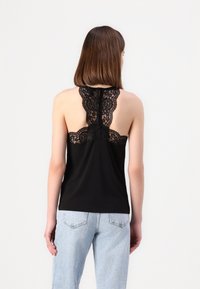 Camiseta sin mangas negra con diseño de espalda de encaje, que presenta un escote redondeado y un dobladillo recto. Combinada con jeans de color azul claro.
