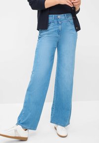 Lichtblauwe wijde jeans gemaakt van denim, met een knoopsluiting en voorkruizen. Gecombinaat met witte sneakers en een marineblauwe trui.