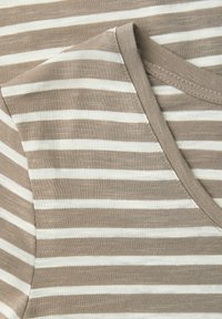 Gros plan sur un tissu à rayures horizontales beige et blanc avec une couture en V au niveau du col et des détails de couture sur les manches courtes.