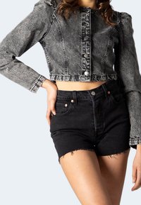 Chaqueta de mezclilla gris recortada con mangas abullonadas y botones plateados, combinada con pantalones cortos de mezclilla negros de tiro alto con dobladillos deshilachados.