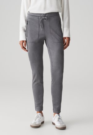 Graue Faux-Suede-Hosen mit einem Kordelzugbund, Reißverschlusstaschen, schmaler Passform und glatter Textur, kombiniert mit weißen Sneakers.