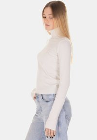 Maglione bianco a collo alto a coste con maniche lunghe, design aderente e texture morbida, abbinato a jeans azzurri a vita alta.