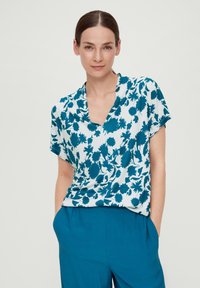 Korte mouw top met een teal bloemmotief op een witte achtergrond, met een V-hals ontwerp en een ontspannen pasvorm. Katoenmix stof.