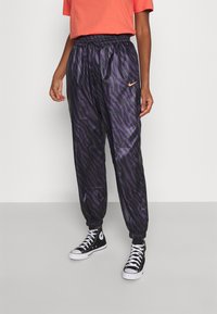Pantaloni della tuta neri e viola a strisce zebrate con vita elastica, caviglie elastiche e un piccolo logo arancione Nike sul lato.