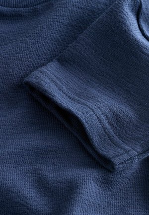 Marineblauwe textuurstof met een geribd patroon, voorzien van een opgevouwen mouw en een glad oppervlak, waarbij de zachte, geweven uitstraling wordt benadrukt.