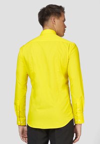 Camicia gialla a maniche lunghe con un design aderente, polsini abbottonati e texture liscia. Presenta un colletto classico e un colore uniforme senza fantasie.