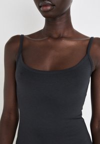 Mustmustähe sobiv tank top õhukeste rihmade ja ümarate kaelustega. Valmistatud siledast venivast kangast. Suumitud ülemise kere lähedalt.