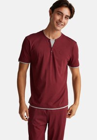 Burgundská halenka s krátkým rukávem typu henley se šedými akcenty, disponující dvěma knoflíky a malým logem na hrudi. Měkký bavlněný materiál.